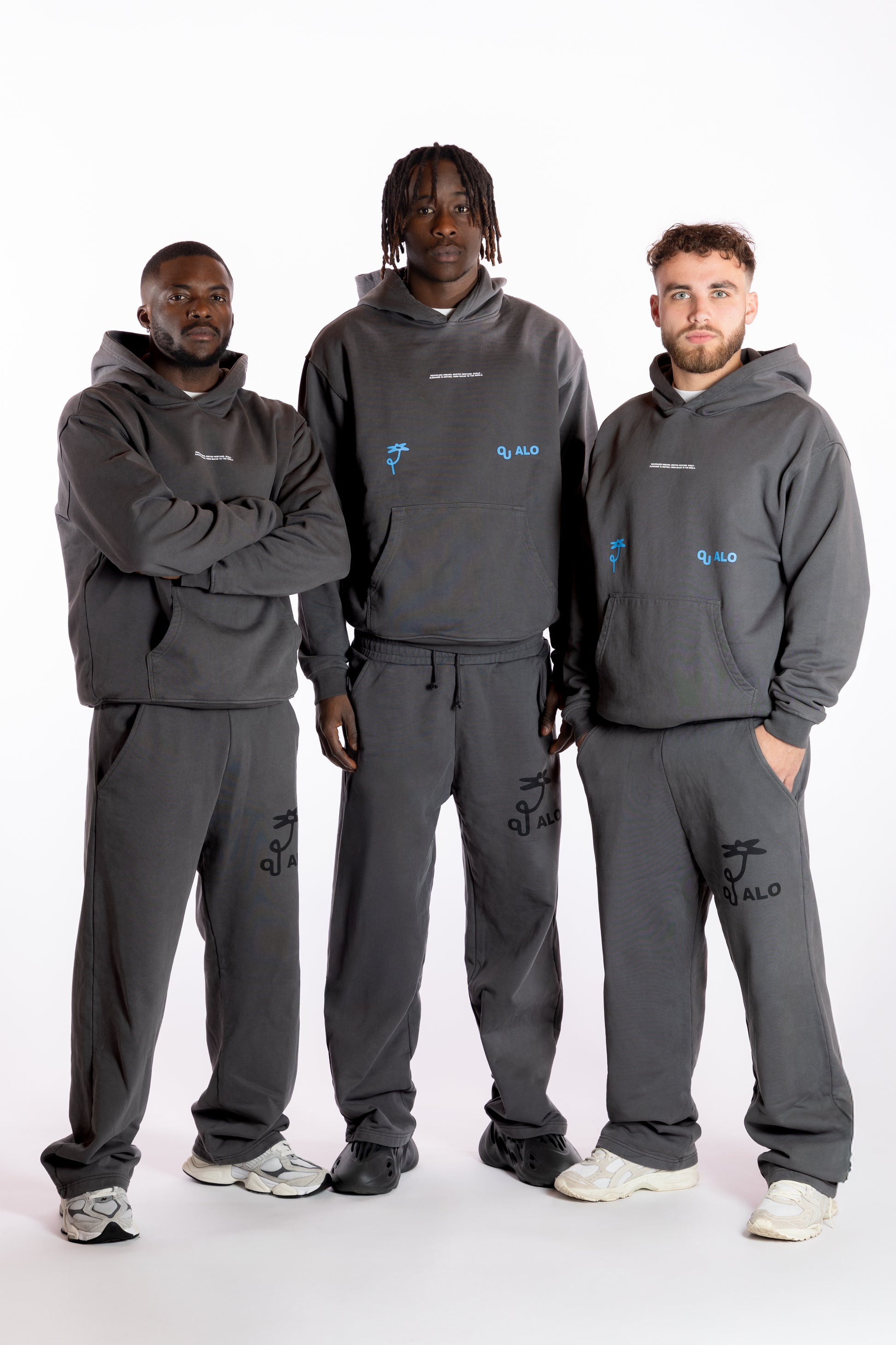 Three individuals wearing matching gray tracksuits with brand logos on a white background