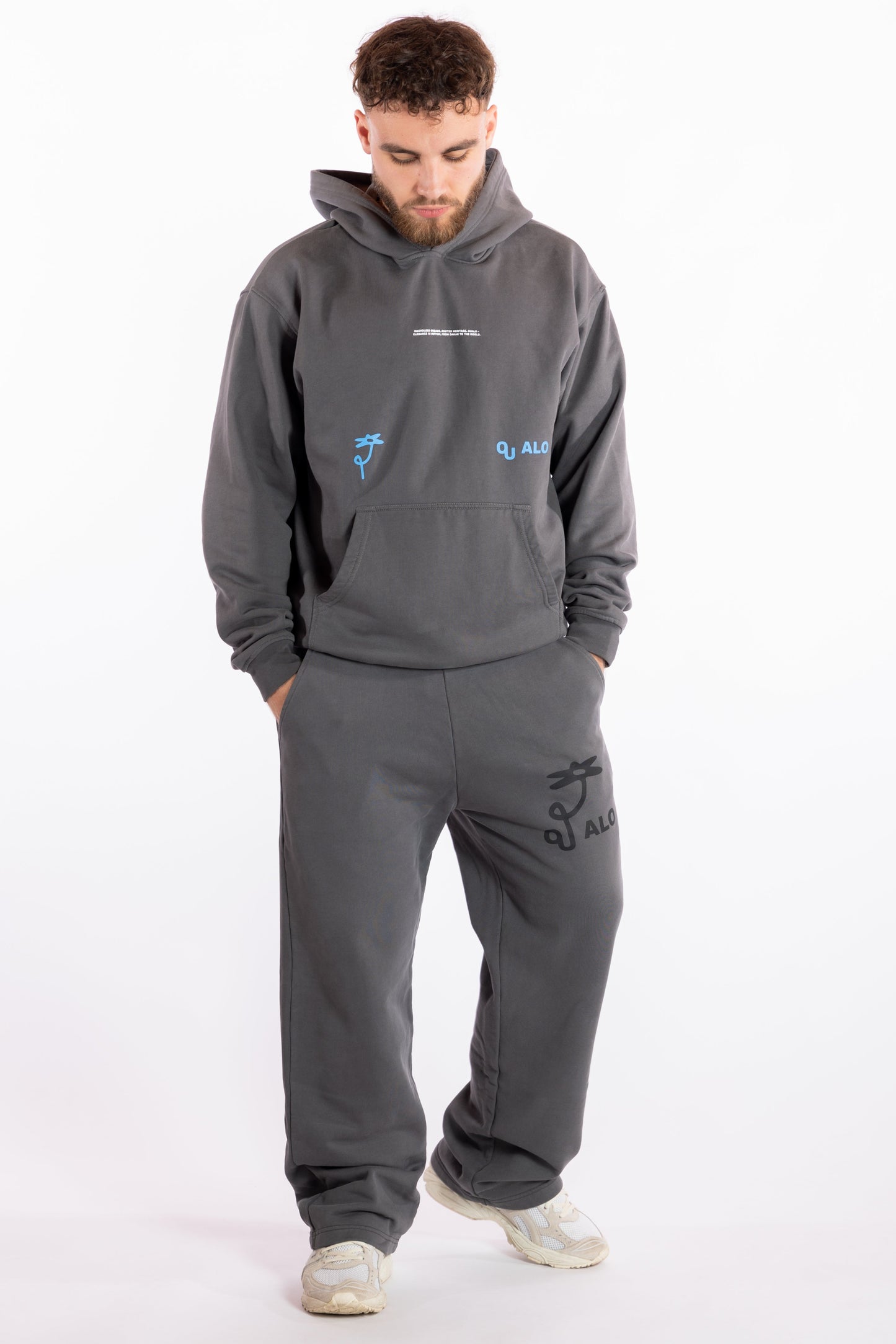 Man wearing a gray hoodie and pants with brand logos on a white background